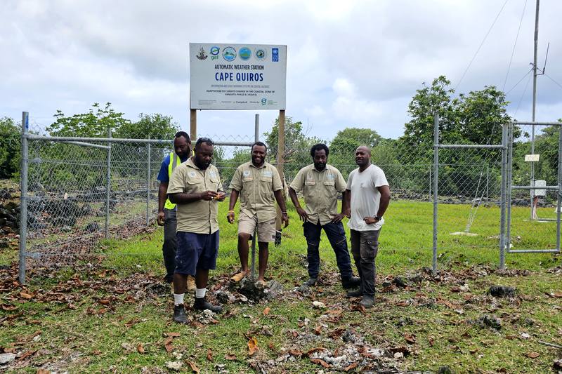 Team standing at the fenced Cape Quiros Automatic Weather Station, with a V-CAP II project sign