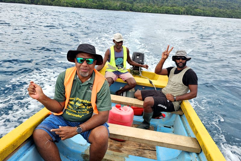 Three men in a small yellow and blue boat travelling at sea