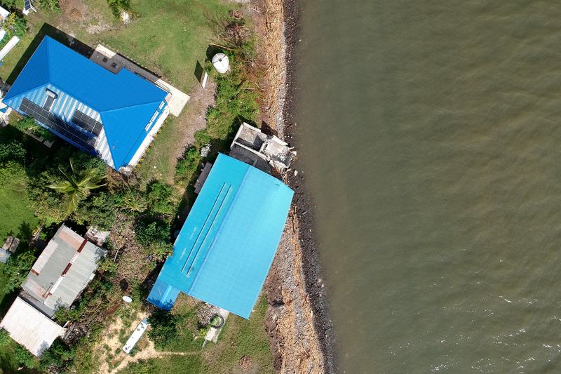 Drone view of coastal houses with blue roofs beside an eroding shoreline