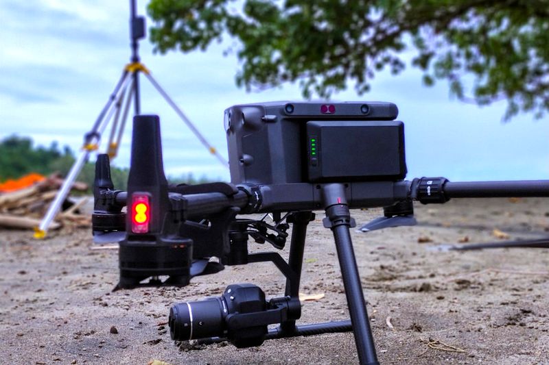 Survey drone with camera set up on the ground beside a tripod