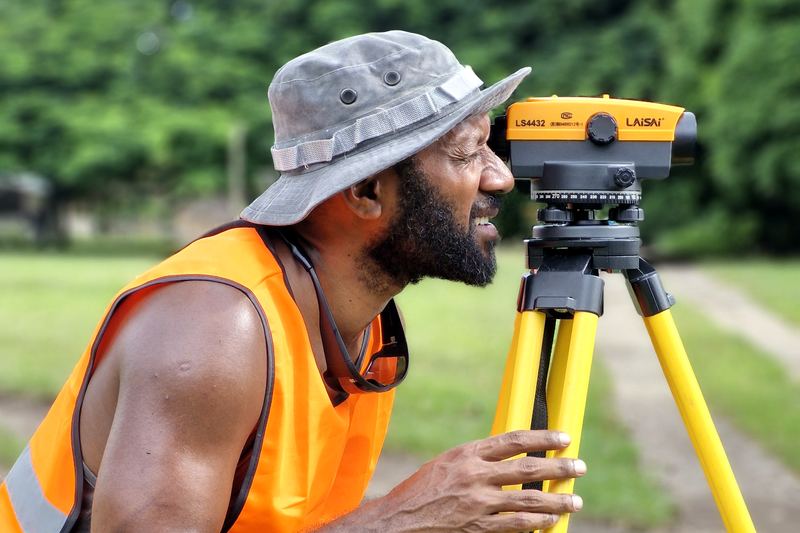 Field technician in a hi-vis vest looking through a survey level on a yellow tripod