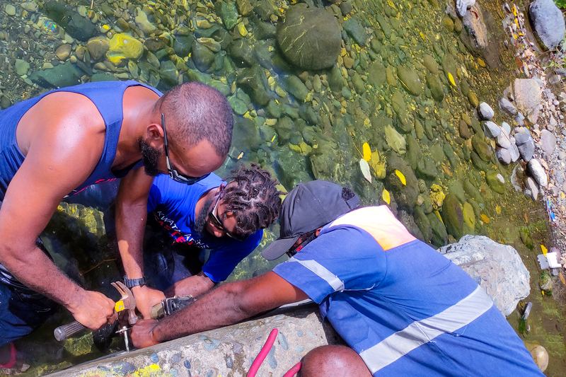 Team members in a clear river installing a gauge on a rock