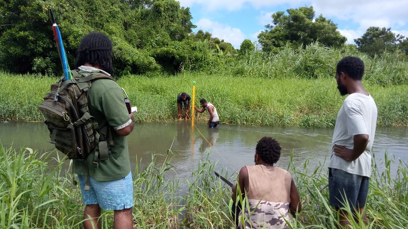 Field team measuring river level with a staff gauge in a shallow stream